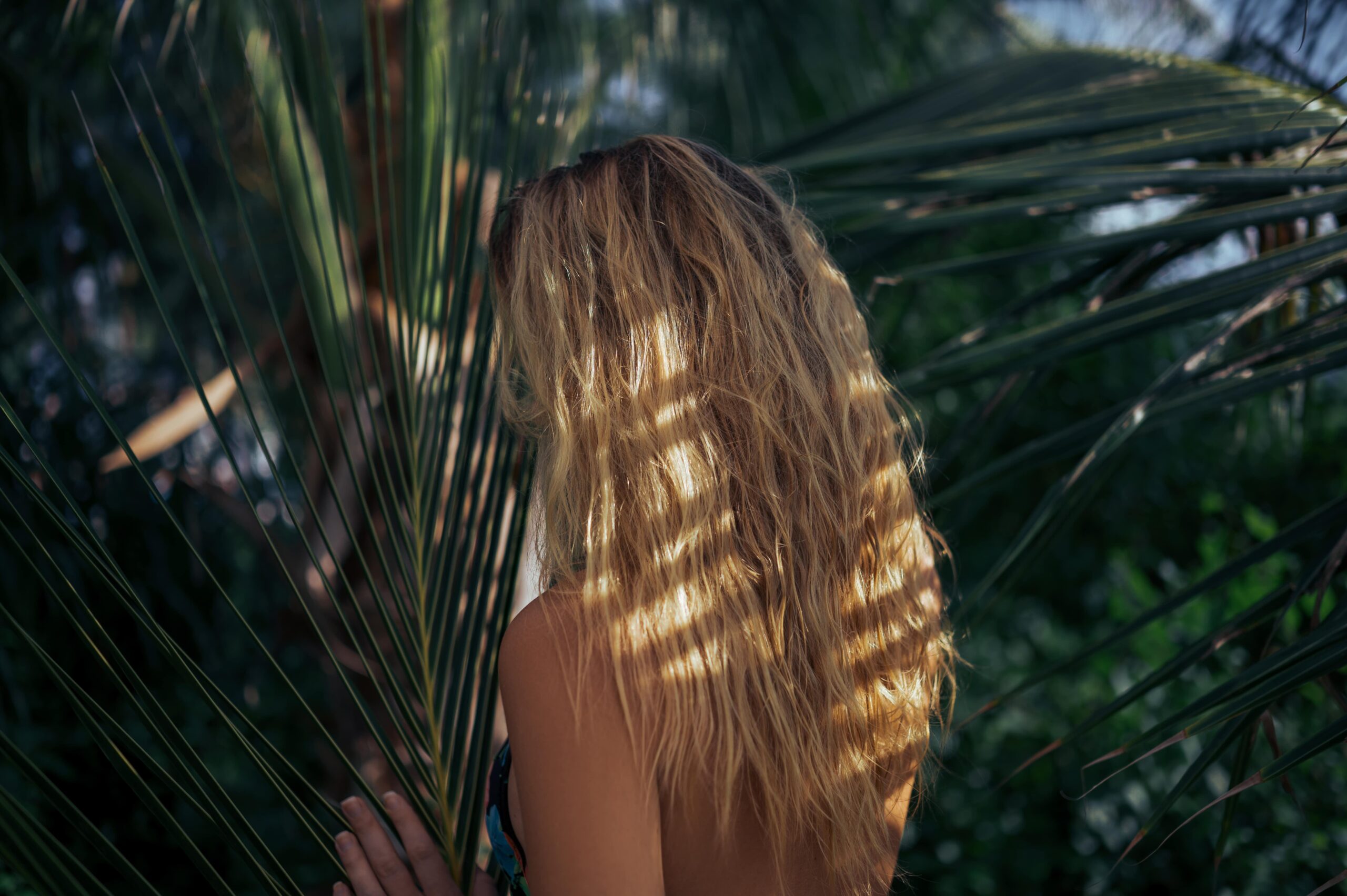 Palm leaves and girl with nice beachy, wavy hair facing away