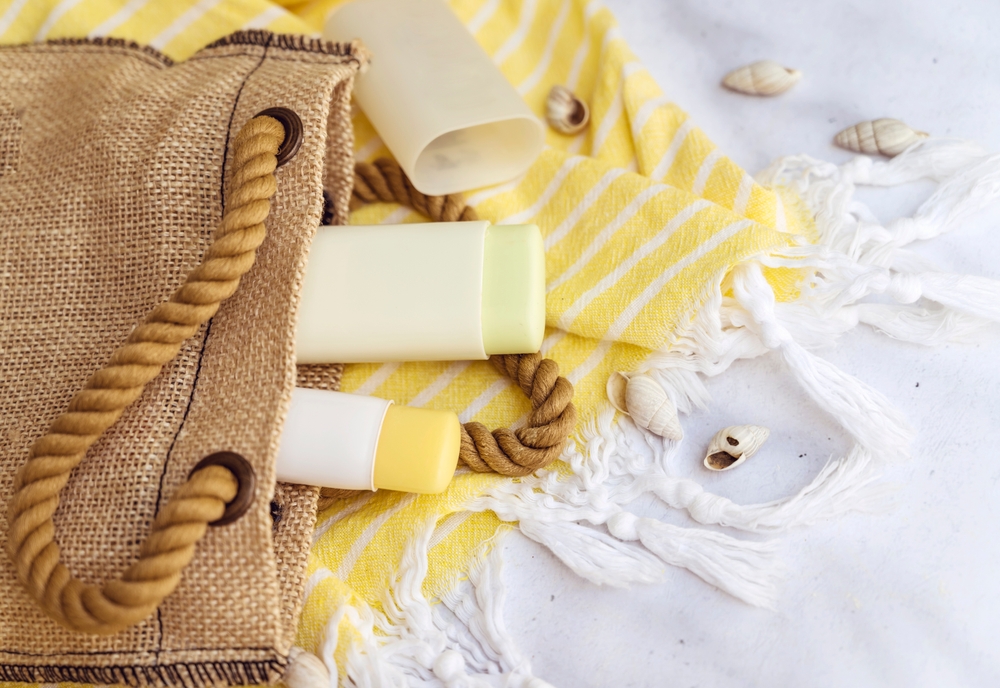 SPF sticks in hessian bag on beach with shells and yellow beach towel