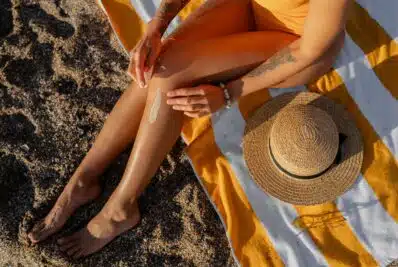 Women's legs on the beach on a striped towel and sun hat placed on the towel.