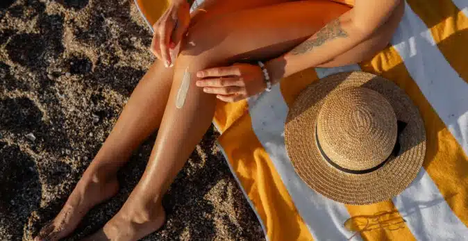 Women's legs on the beach on a striped towel and sun hat placed on the towel.